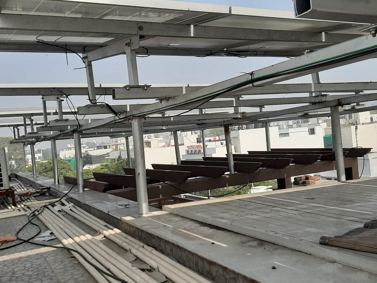 Steel mounting structure under construction on a rooftop, with panels fitted overhead and rails stacked below.