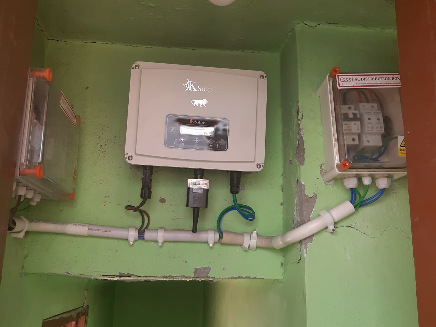 Wall-mounted KSolare 5G Pro inverter between a junction box and an AC distribution box on a green wall.