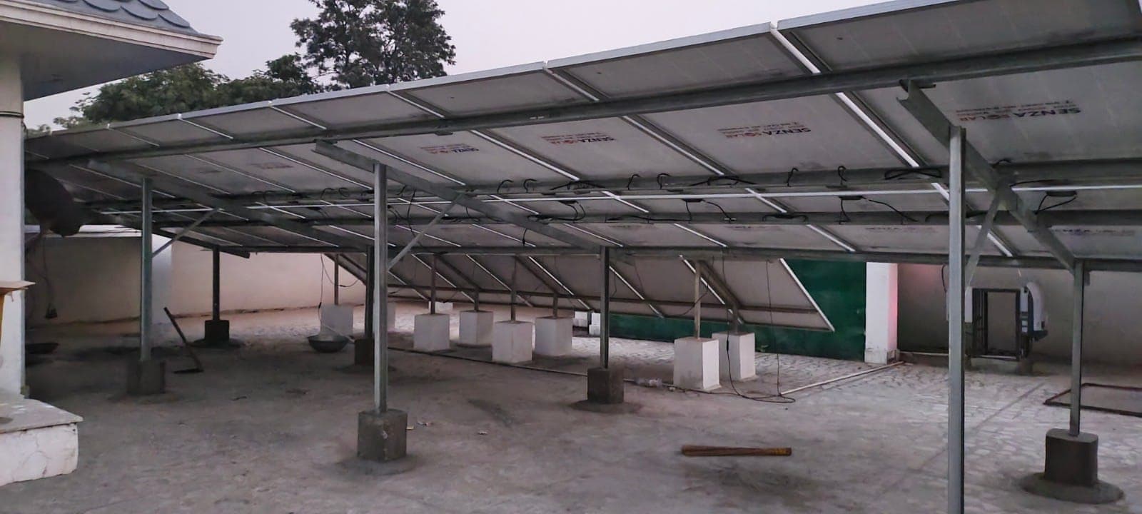 Wide view beneath an elevated rooftop solar structure with steel posts on concrete footings at dusk.