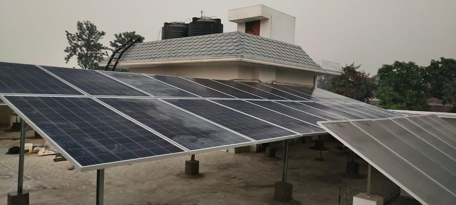 Rows of blue solar panels on a low steel structure across a flat rooftop with water tanks behind.