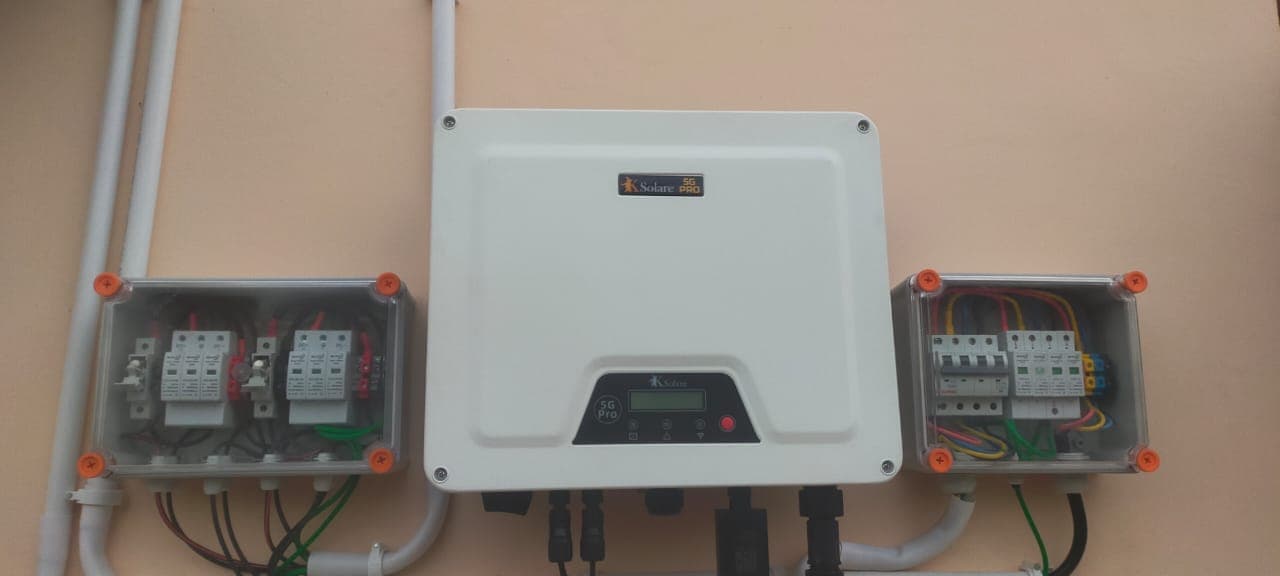 KSolare 5G Pro inverter mounted on a peach wall between two clear-lidded junction boxes with breakers and surge protectors.