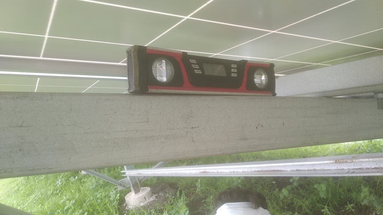 Red digital spirit level resting on a galvanised steel beam beneath solar panels
