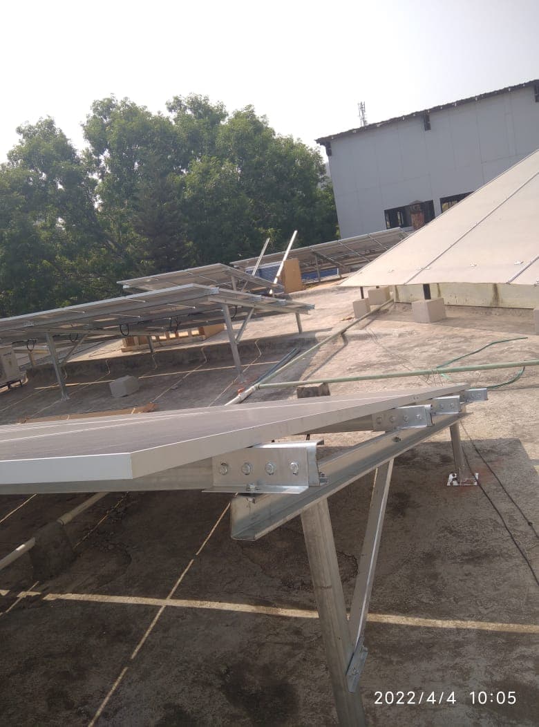 Galvanised steel mounting frame with one panel fixed on a flat rooftop beside a sloped roof section