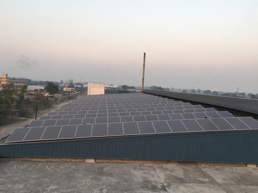 Large array of solar panels covering a sloped metal shed roof at dusk under a hazy sky