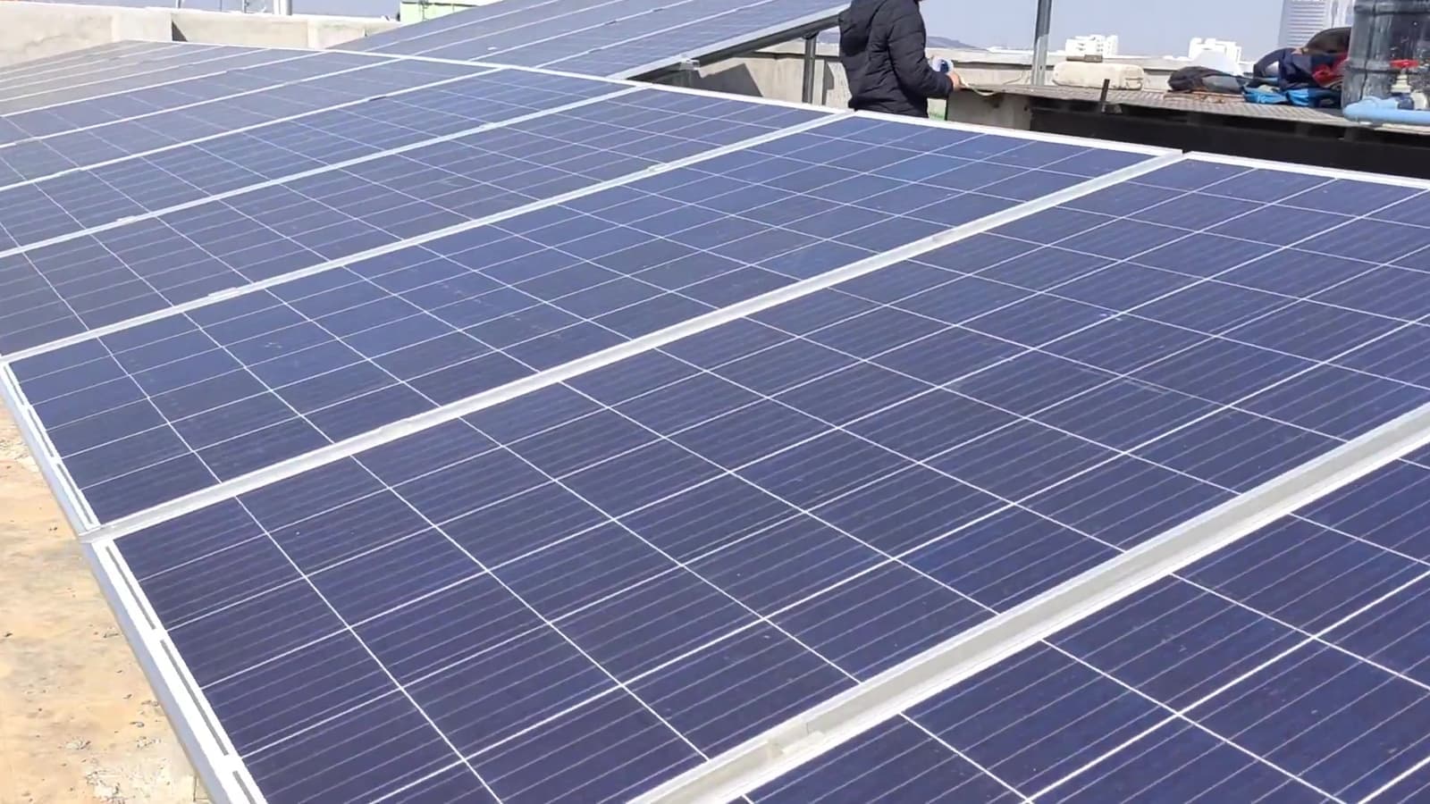 Close-up of polycrystalline solar panels on a rooftop with a worker standing beyond the array