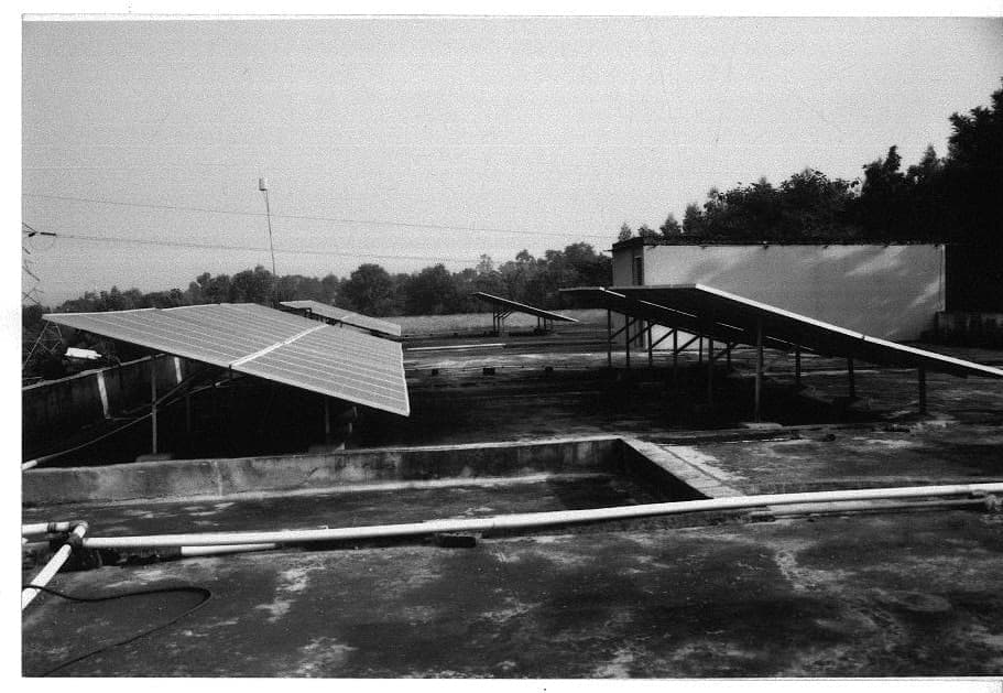 Black-and-white photograph of tilted solar arrays on steel frames across a flat concrete roof
