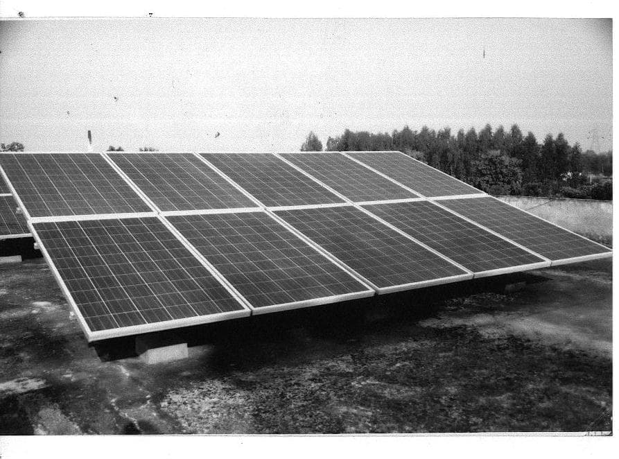 Black-and-white photograph of two rows of solar panels on low mounts on a flat roof