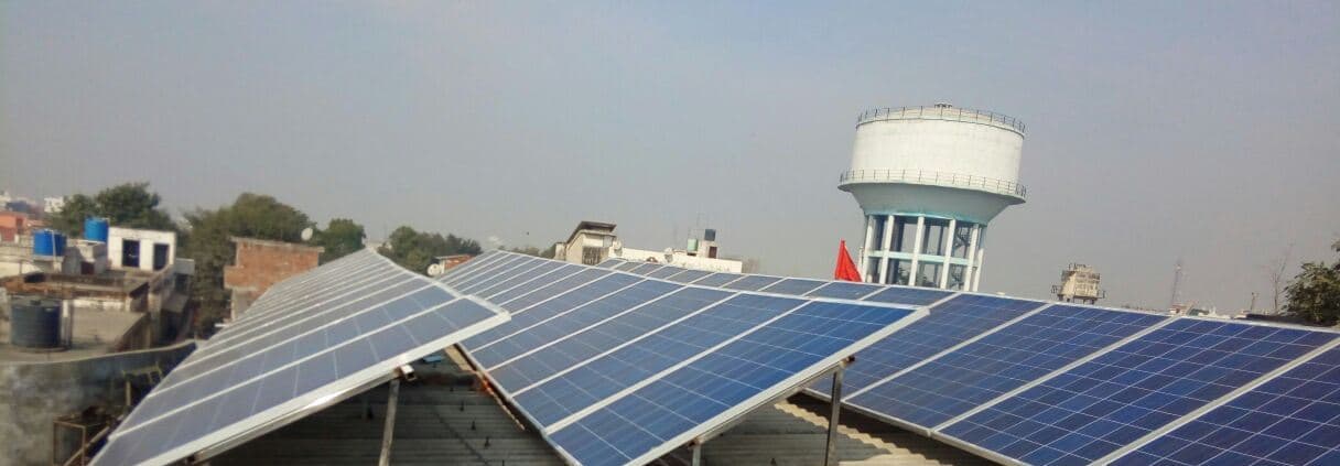 Rows of solar panels on a corrugated metal roof with a water tower rising behind