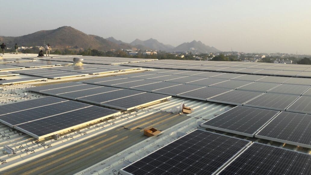 Solar panels being fitted on a corrugated industrial roof with hills and a town in the distance