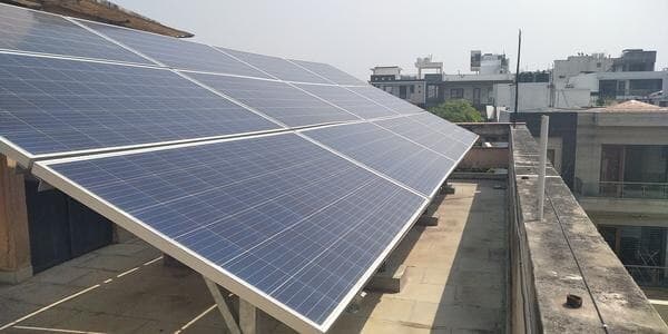 Solar panels on a raised steel frame above a house rooftop with neighbouring buildings behind