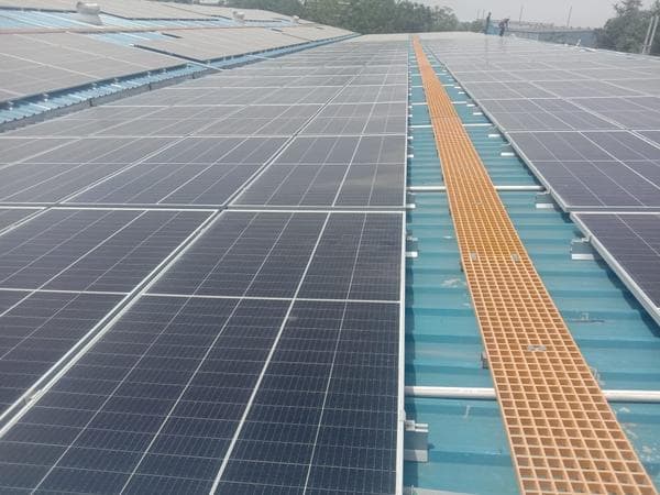 Solar panels on a blue metal industrial roof with an orange grating walkway between rows