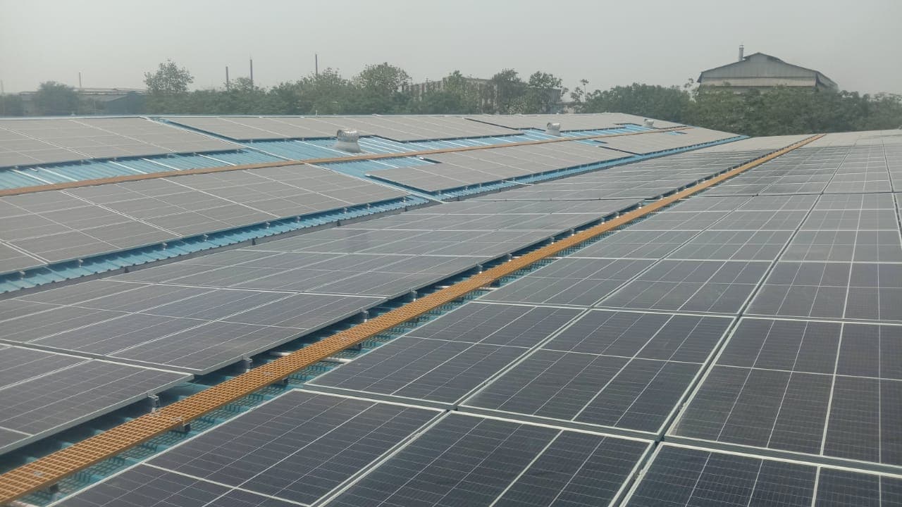 Wide view of a large rooftop solar array on a blue metal roof with orange grating walkways