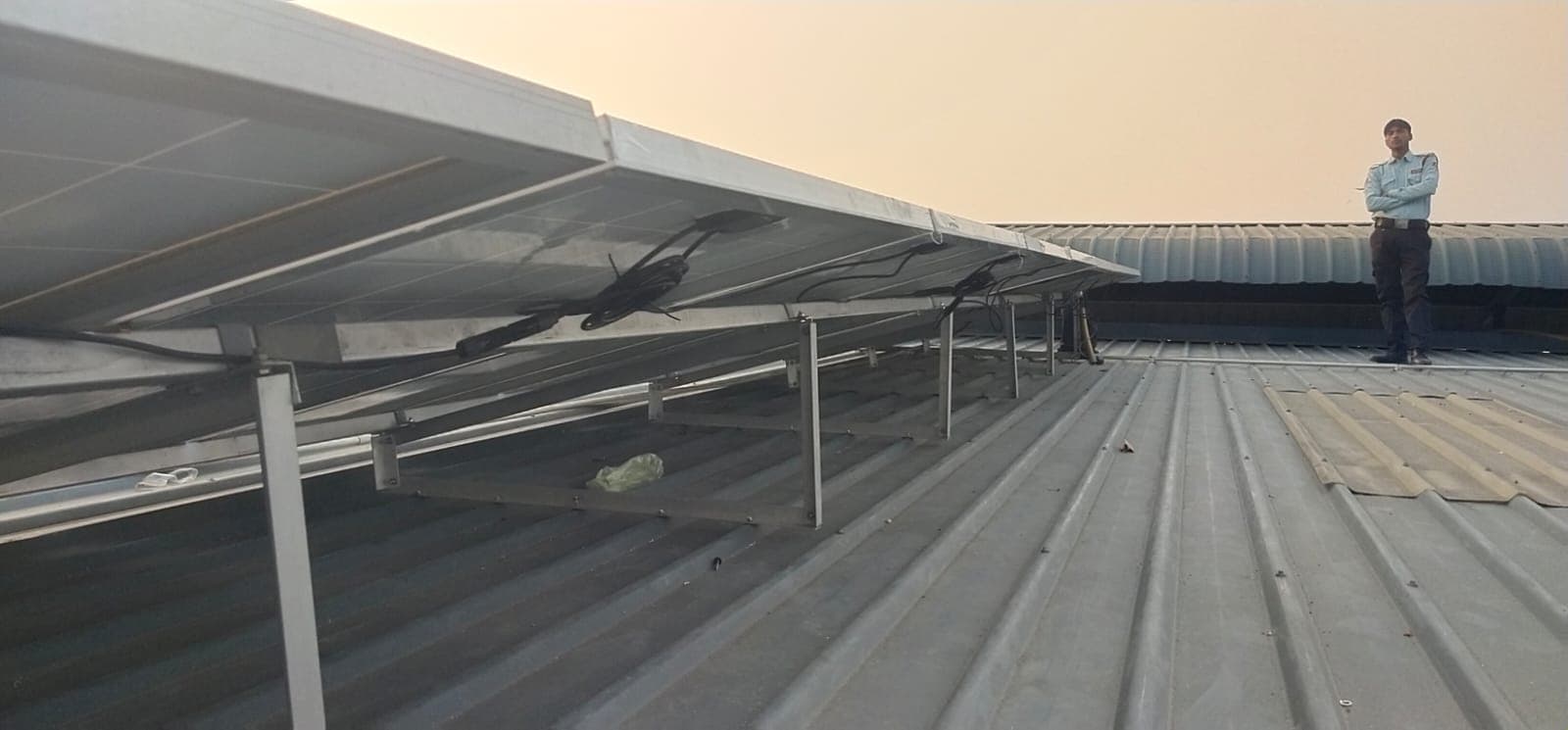 Underside of solar panels on aluminium rails over a corrugated metal roof, with a uniformed man standing nearby