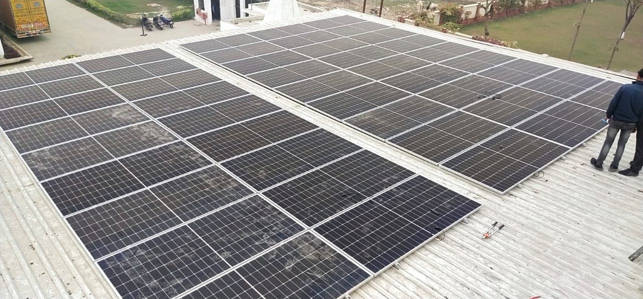Two blocks of solar panels on a corrugated metal roof, with two workers standing at the edge