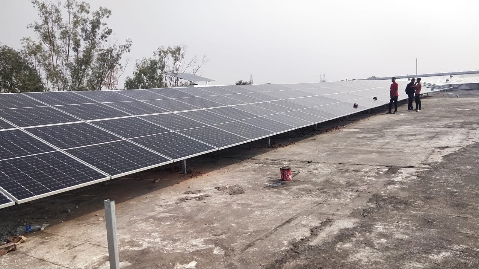 Long row of tilted solar panels on low steel posts across a flat concrete rooftop under a hazy sky