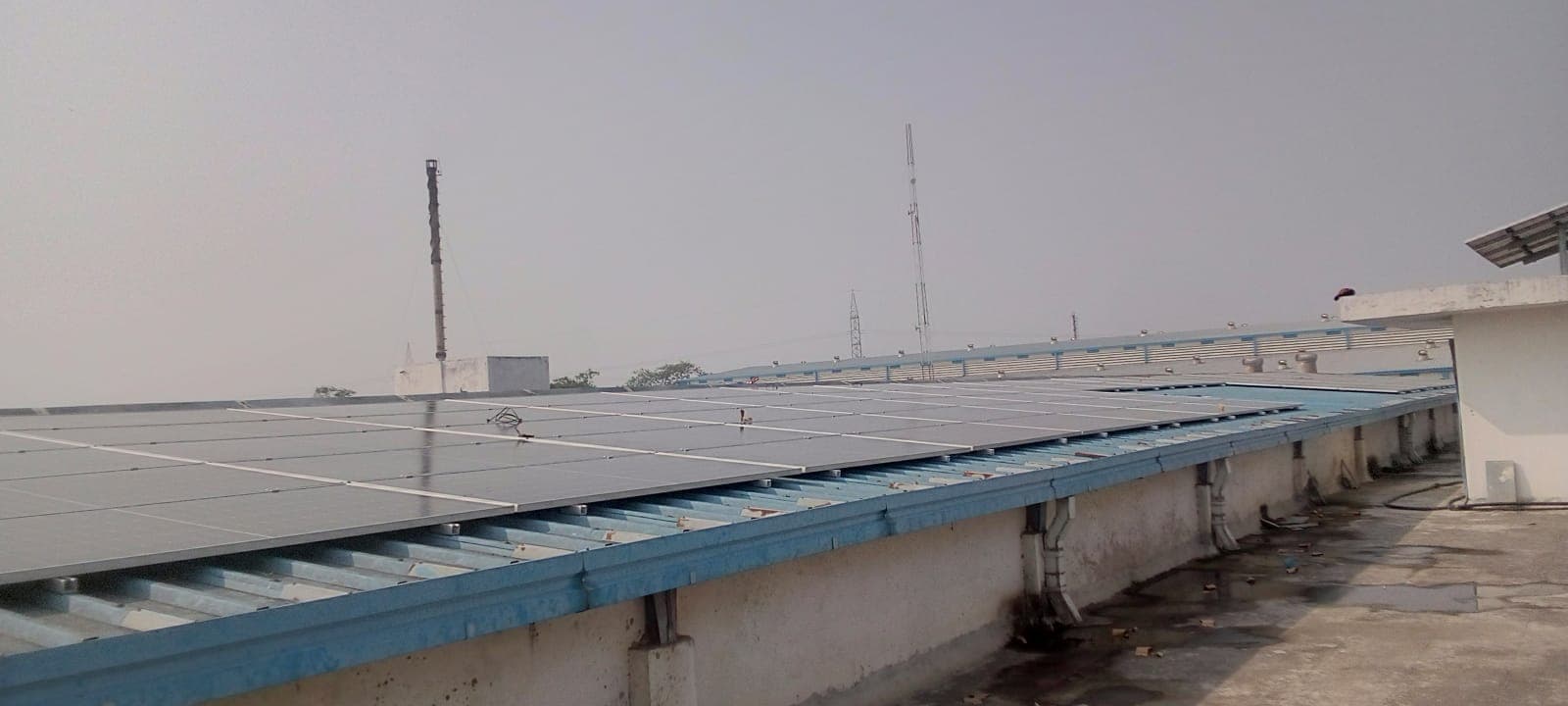 Rows of solar panels on blue steel rails over a corrugated roof beside a concrete walkway