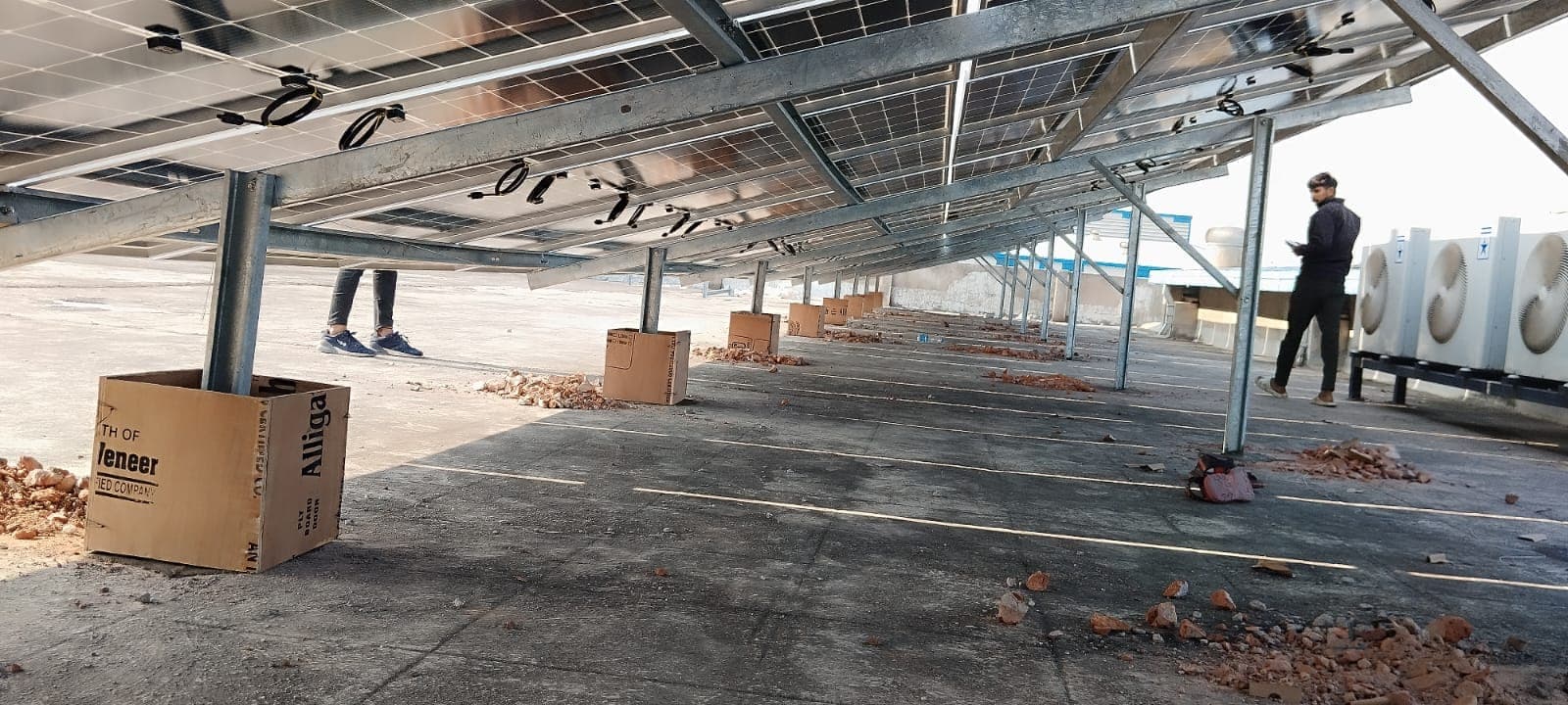 Galvanised steel posts and rails supporting solar panels above a flat concrete roof, with a worker standing beneath