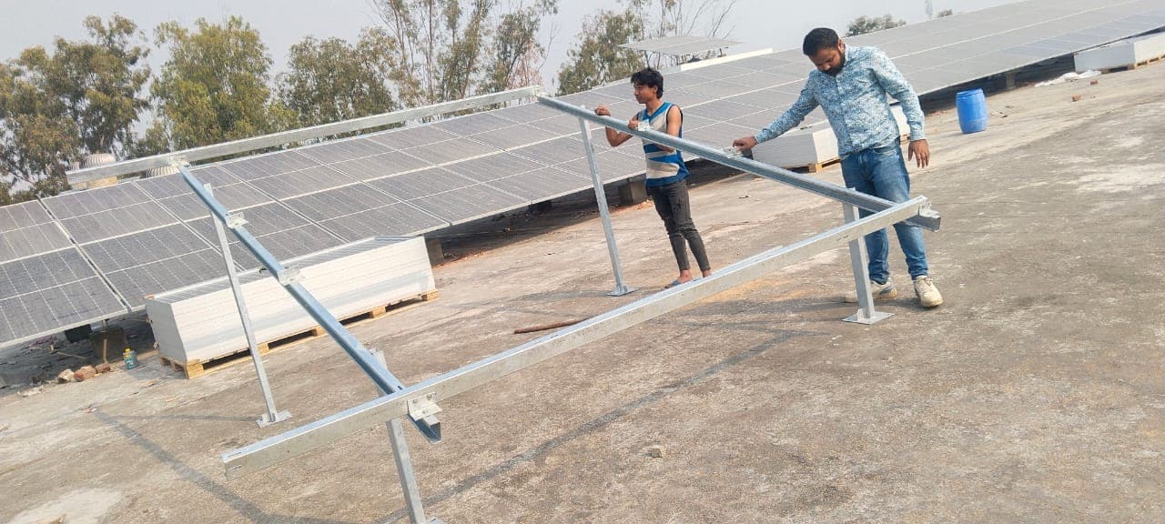 Two workers assembling a galvanised steel solar mounting frame on a flat roof with panel rows behind