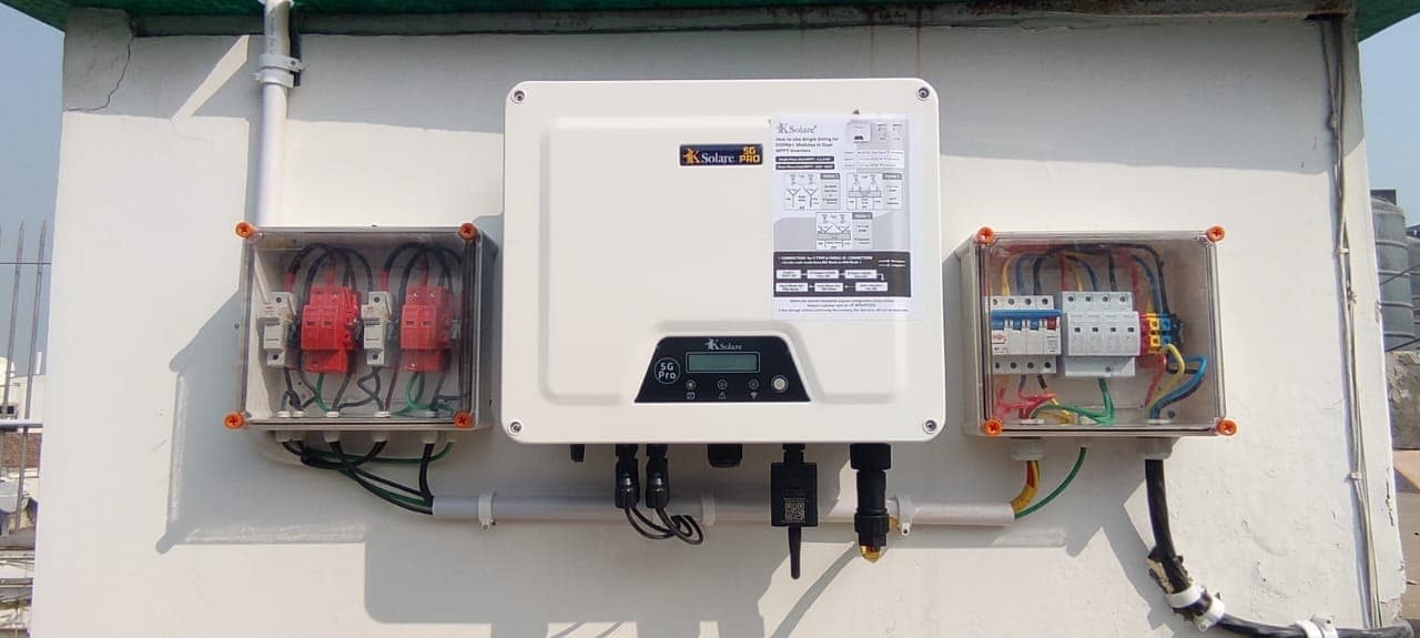 Wall-mounted KSolare 5G Pro solar inverter between two clear-lidded switchgear boxes on a white wall