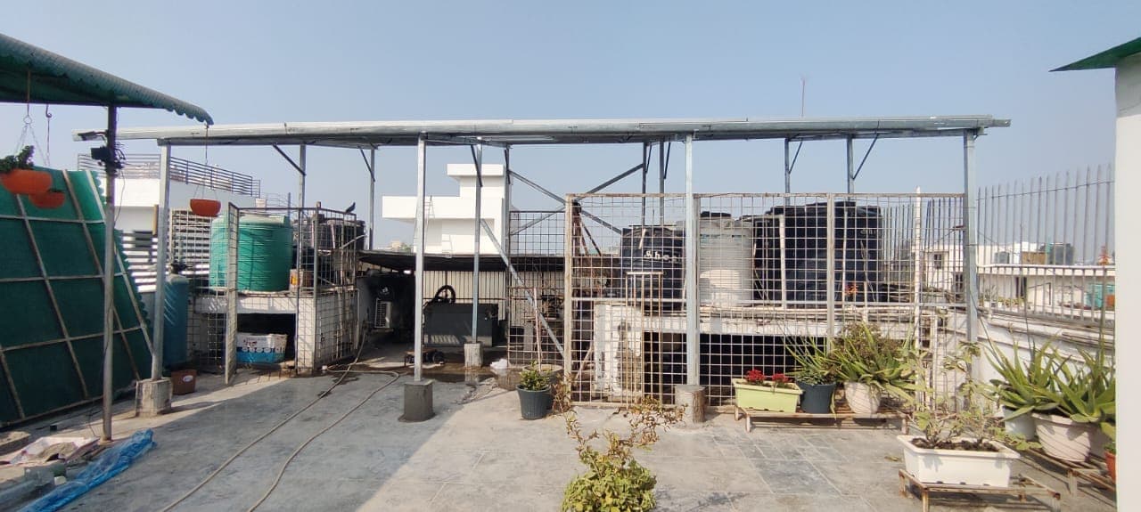 Galvanised steel elevated frame over a residential rooftop terrace with water tanks and potted plants