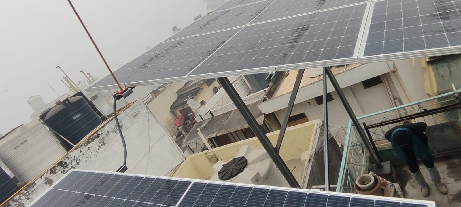 Underside view of solar panels on a raised steel frame over a rooftop with neighbouring houses below