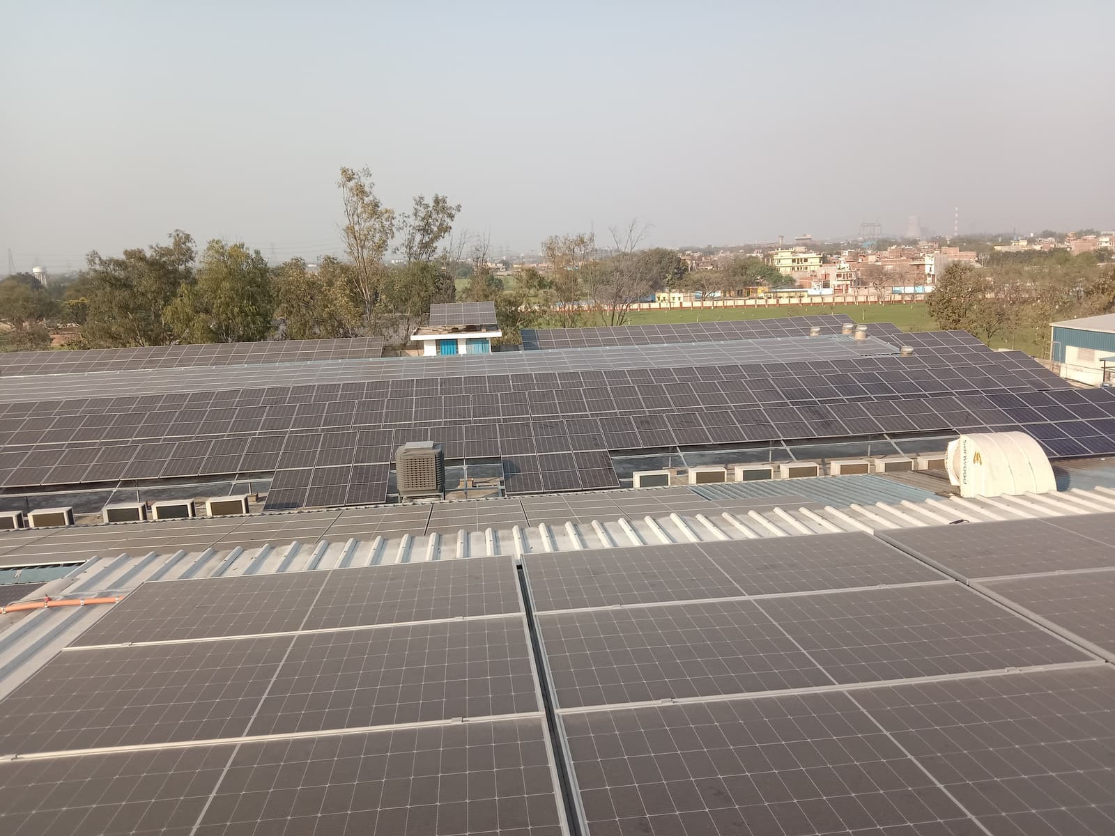 Rows of solar panels across a large industrial rooftop with a town and trees in the distance