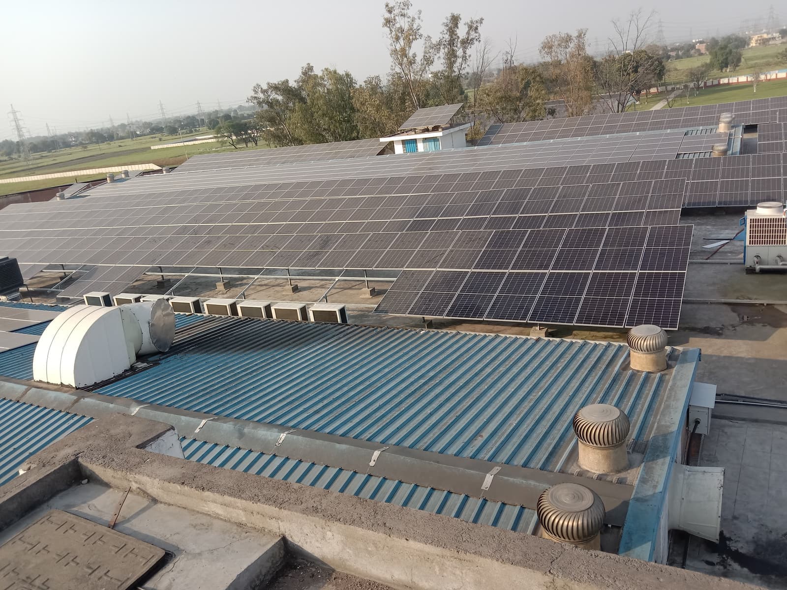 Solar panel rows on a factory roof behind a blue corrugated section with turbine ventilators