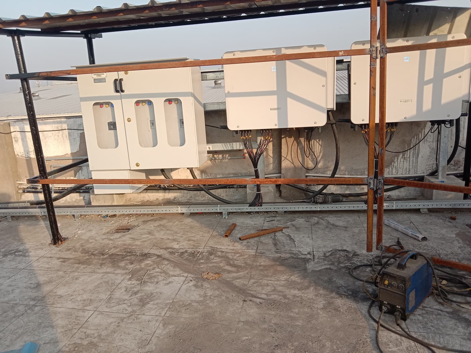 Two Sungrow inverters and a distribution panel under a rooftop shed with a steel frame being built
