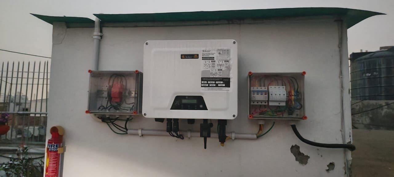 Wall-mounted KSolare 5G Pro solar inverter between two transparent DC and AC distribution boxes on a rooftop wall