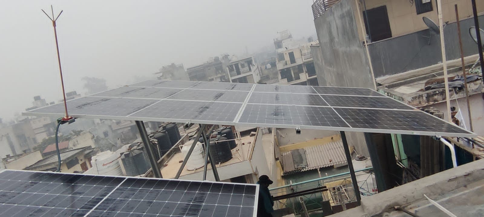 Solar panel array on an elevated structure above dense rooftops and water tanks in hazy weather