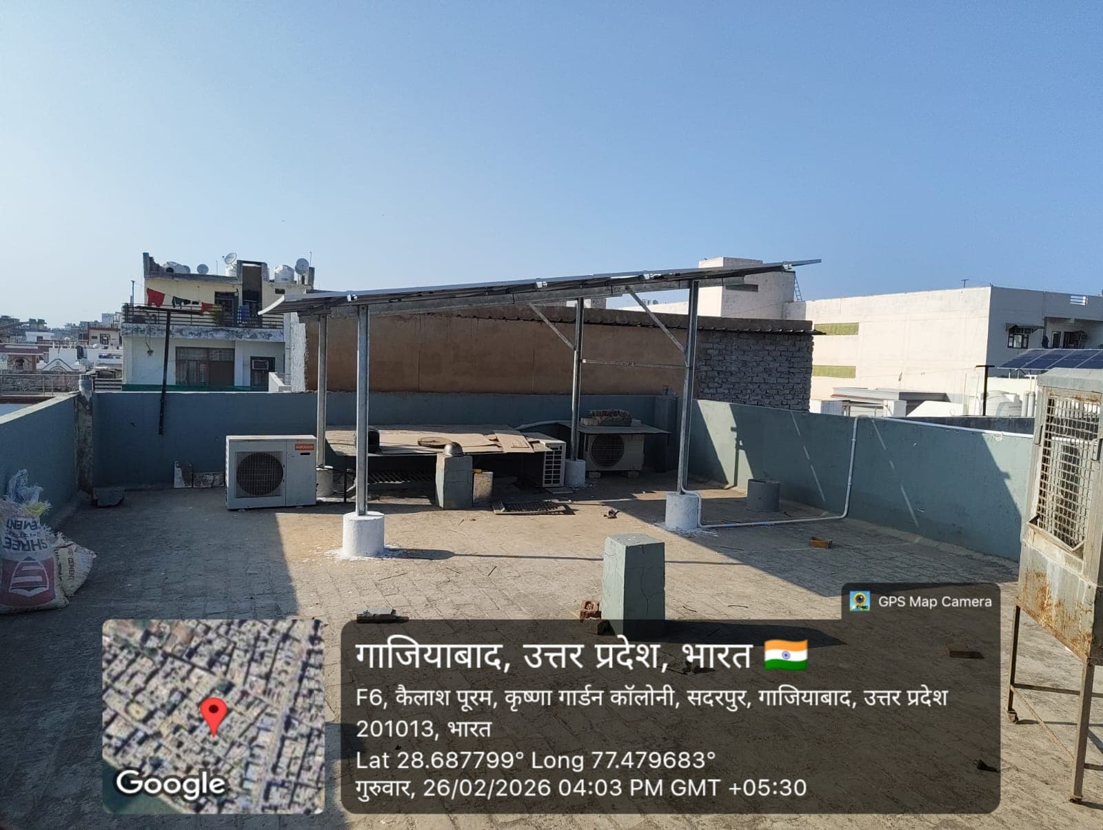 Elevated solar panel structure on galvanised steel columns above a rooftop terrace with air-conditioner units