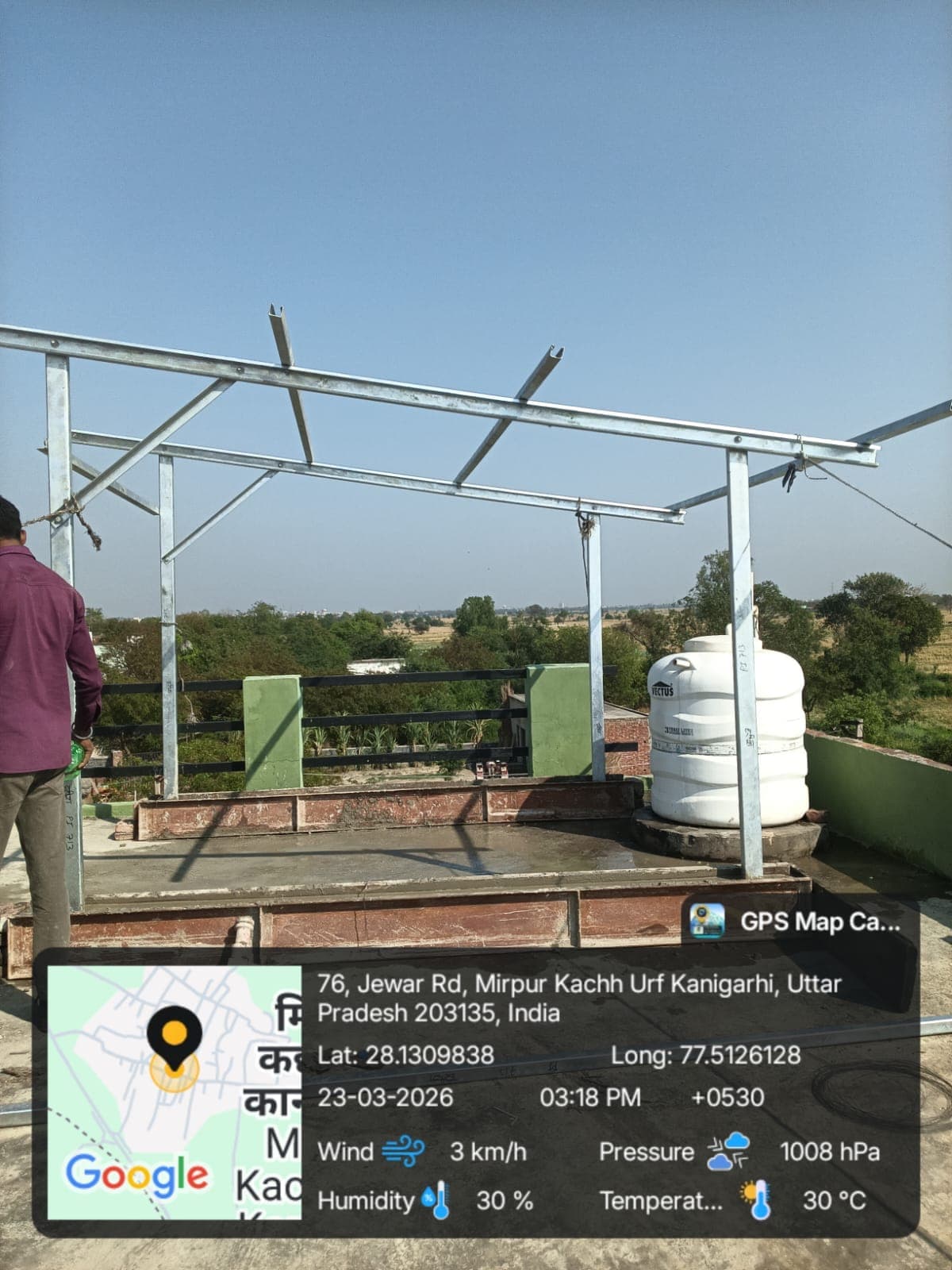 Galvanised steel solar mounting frame with angled rails on a rooftop beside a white water tank and open fields