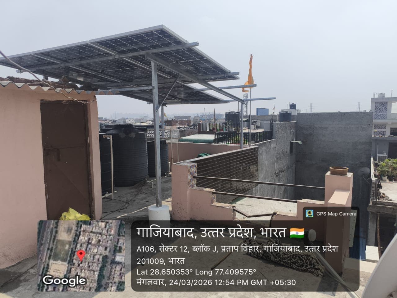 Solar panels on an elevated steel structure above a residential rooftop with water tanks in Ghaziabad