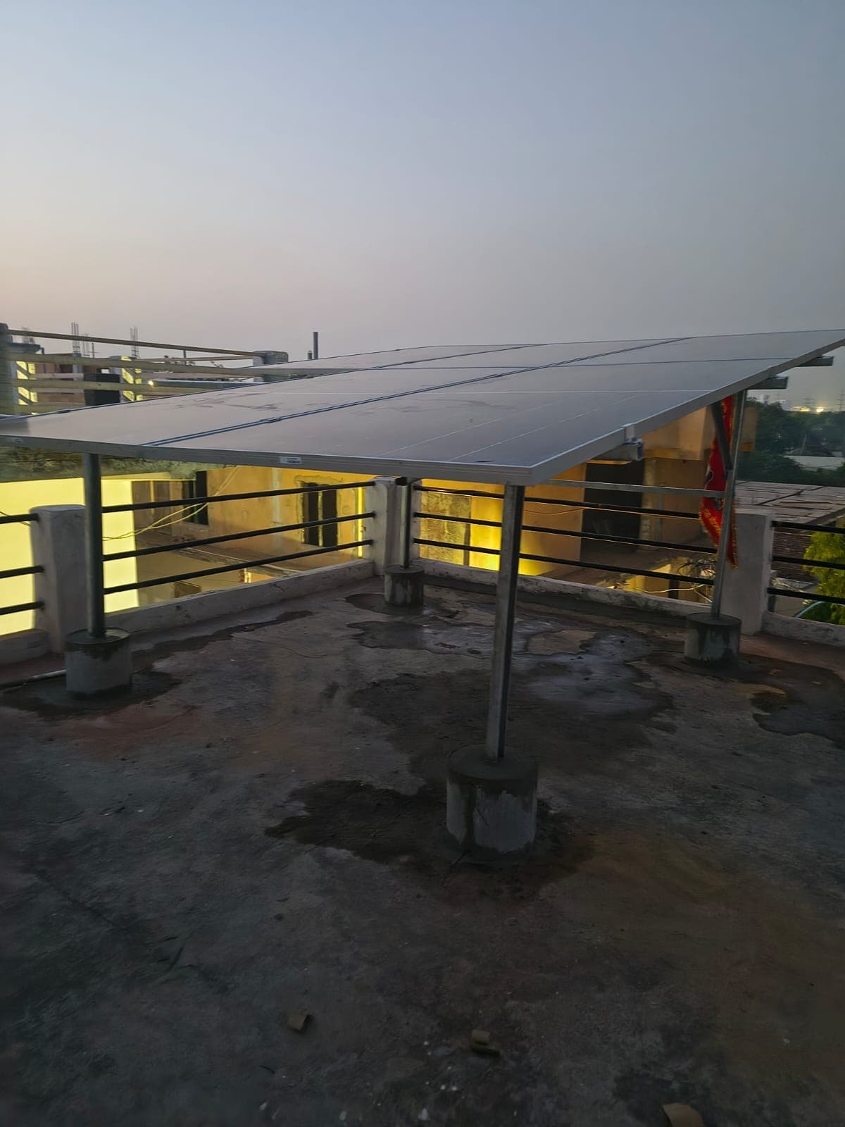 Elevated solar panel canopy on steel posts with concrete footings on a bare rooftop at dusk