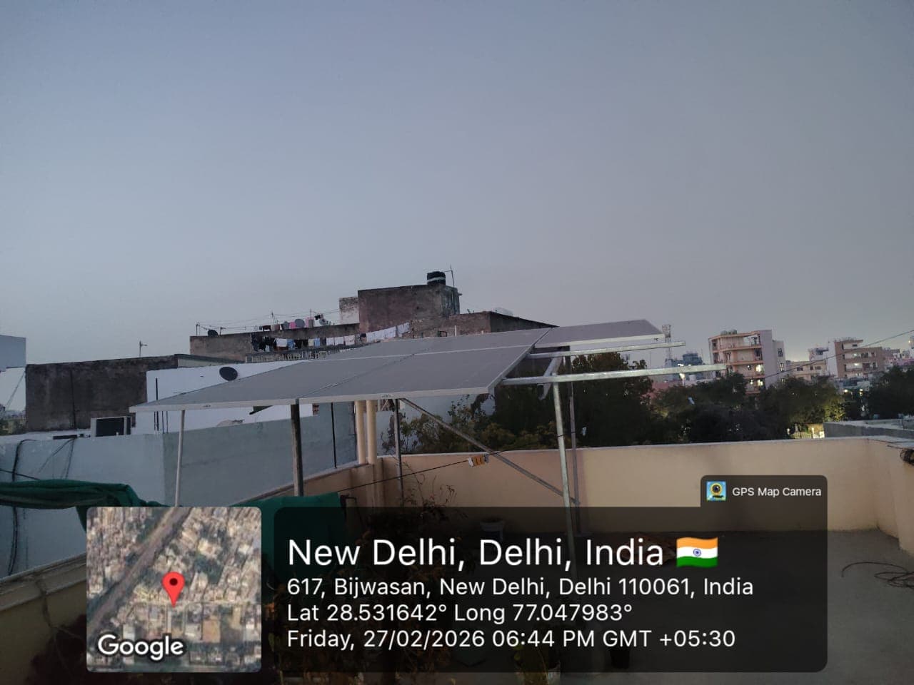 Solar panels on an elevated steel frame above a rooftop parapet against a dusk sky in New Delhi