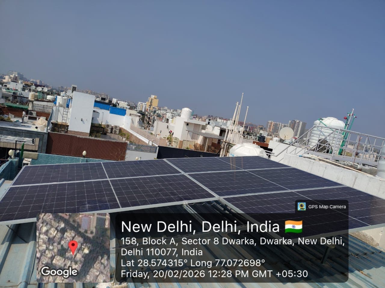 Rows of solar panels mounted low over a corrugated metal roof with a sunny city skyline behind in New Delhi