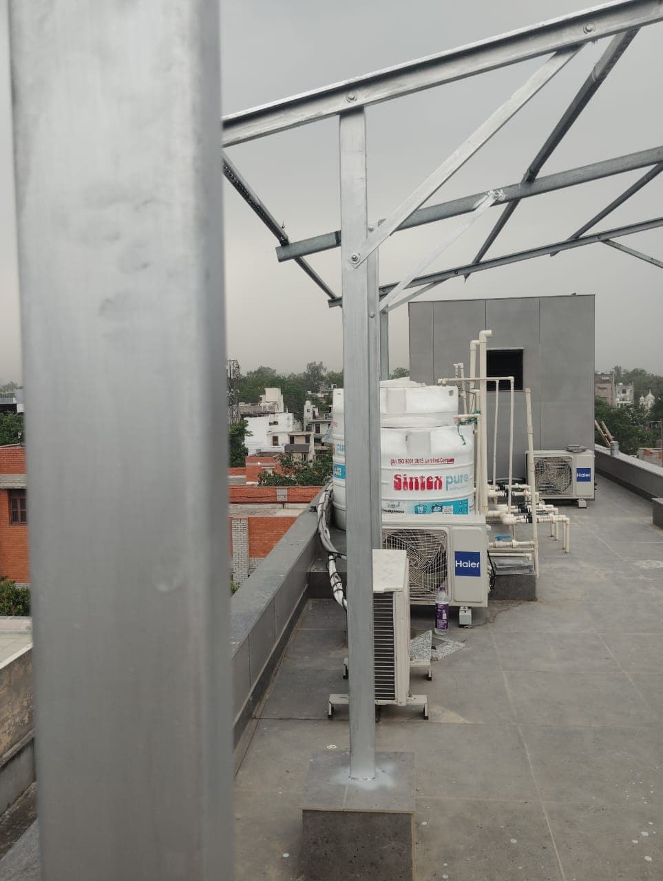 Galvanised steel mounting structure awaiting panels beside water tanks and air-conditioner units on an overcast rooftop