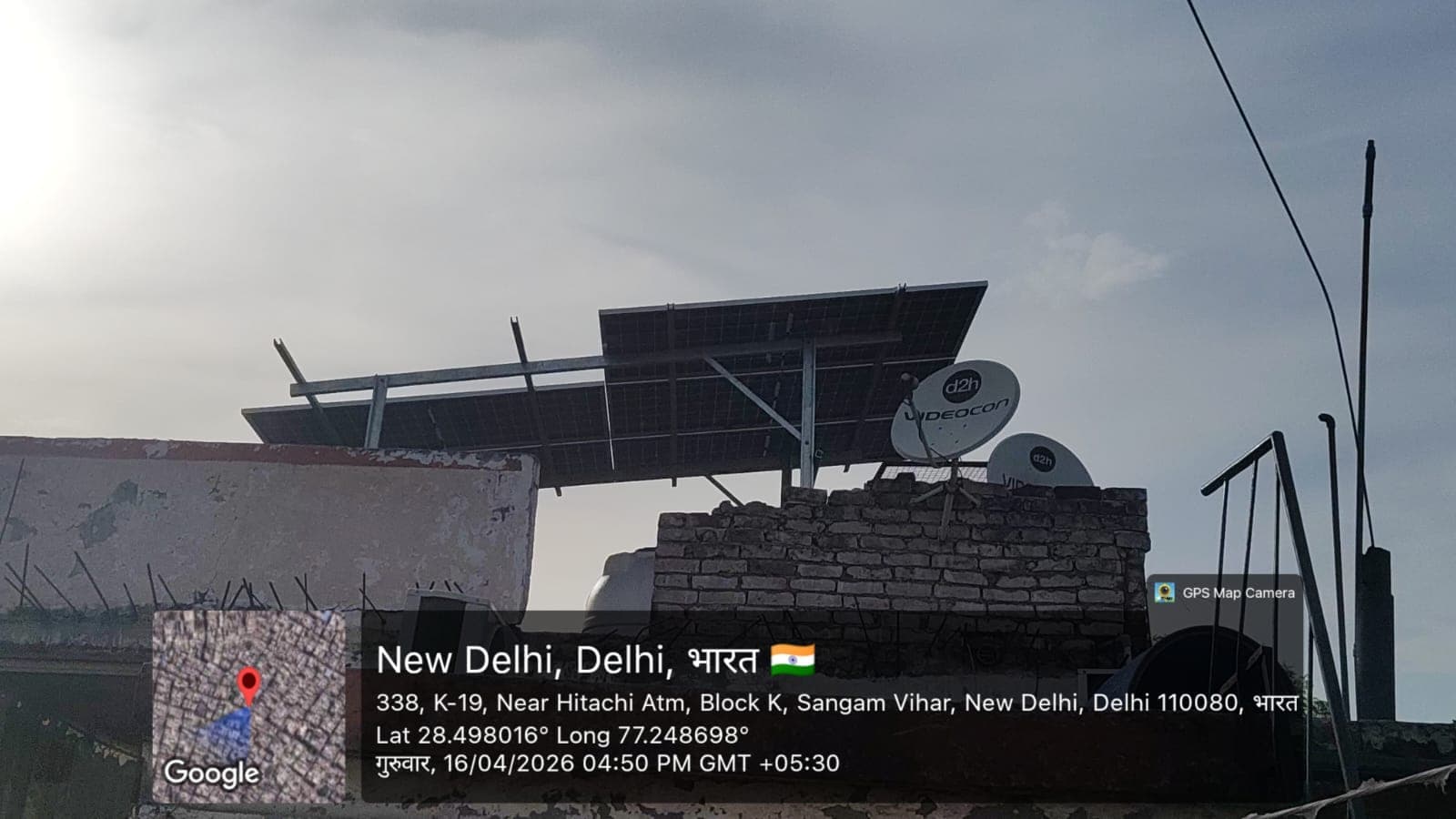 Small elevated solar array on a steel frame beside two satellite dishes above a brick parapet in New Delhi